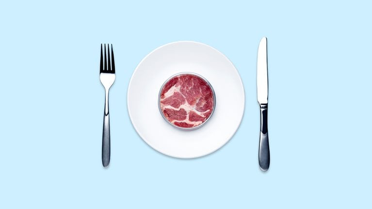 Overhead view of lab grown meat in a Petri dish served on a white plate on a light blue table.